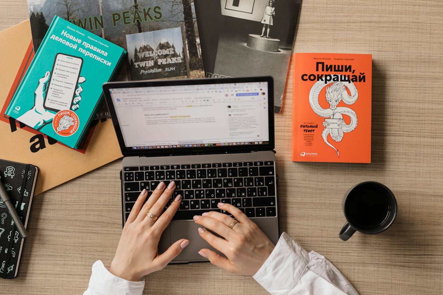 Hands typing on a laptop surrounded by books and coffee.